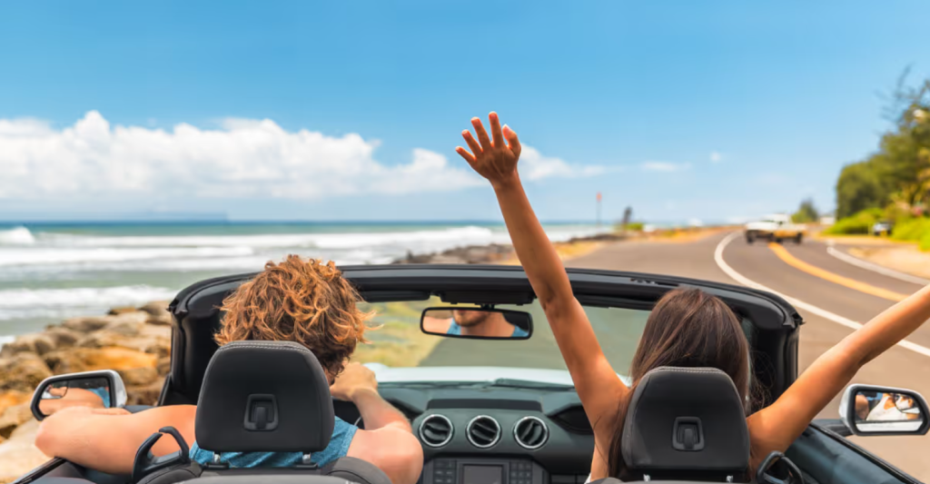 Couple driving a convertible along a scenic coastal highway on a sunny day, enjoying a summer road trip with the top down symbolizing the freedom of travel in a well-maintained vehicle. Schedule your service at Summerville Ford!